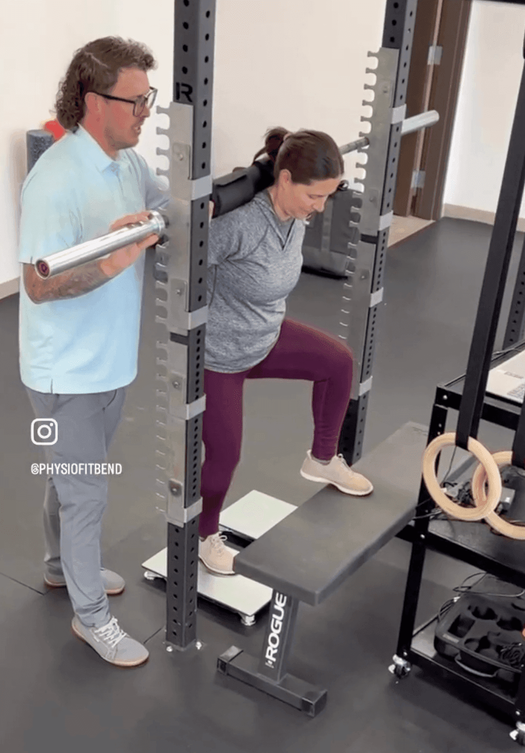 Side profile view of a woman performing a weighted step-up on force plates. This angle highlights the alignment of the knee over the toe and torso positioning while a trainer spots the lift.