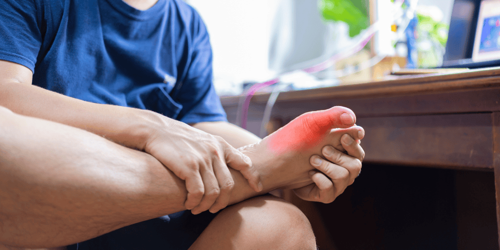 Man sitting in front of his desk holding his foot in pain.