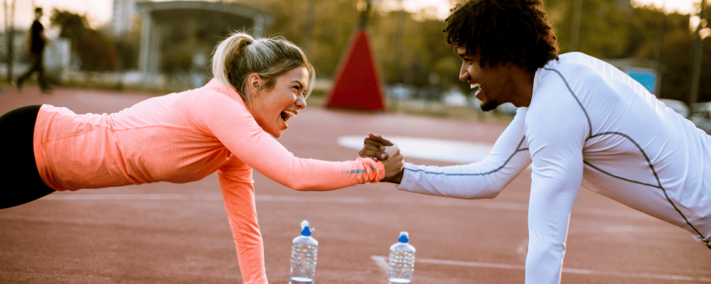 A man and woman doing a plank on one hand outside while holding eachother's hand.