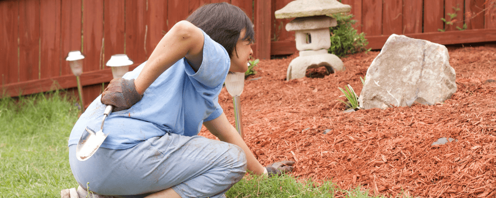 Woman outside gardening, bent down, and holder her low back in pain.